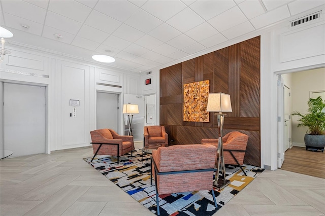 living room with visible vents, wooden walls, and elevator