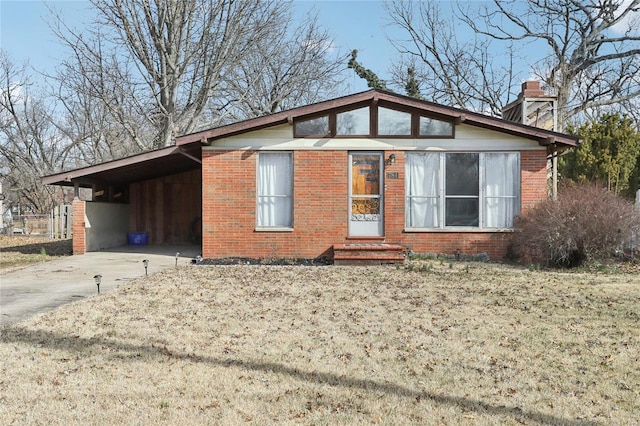 view of side of home featuring an attached carport, driveway, a chimney, entry steps, and brick siding