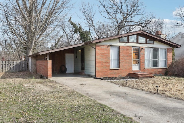 view of side of home with a carport, fence, brick siding, and driveway