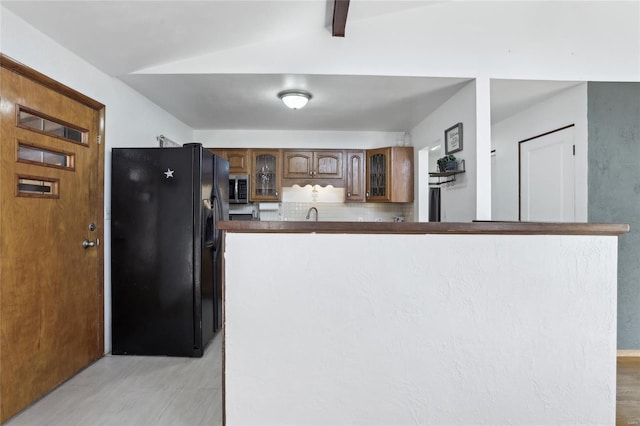 kitchen featuring dark countertops, decorative backsplash, glass insert cabinets, stainless steel microwave, and black refrigerator with ice dispenser