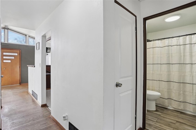 interior space featuring visible vents, curtained shower, baseboards, toilet, and wood finished floors