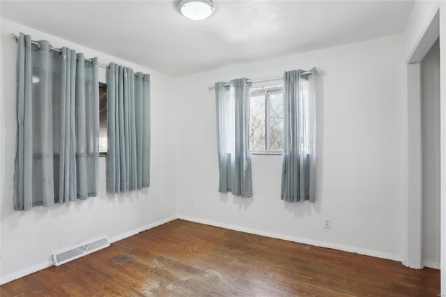 empty room with wood finished floors, visible vents, and baseboards