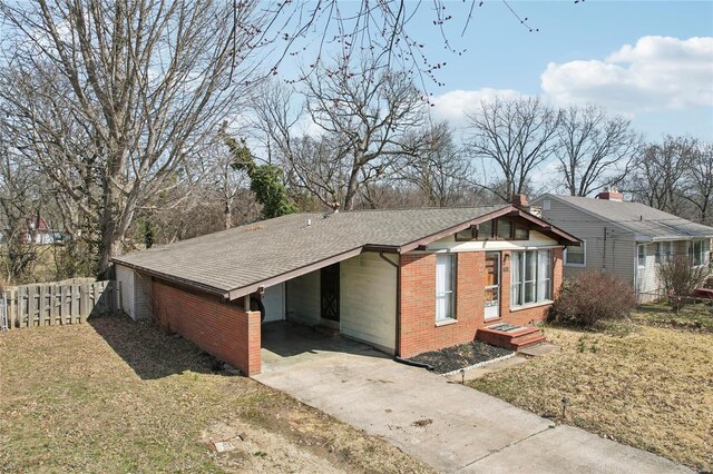 view of side of home with brick siding, a shingled roof, fence, concrete driveway, and a carport