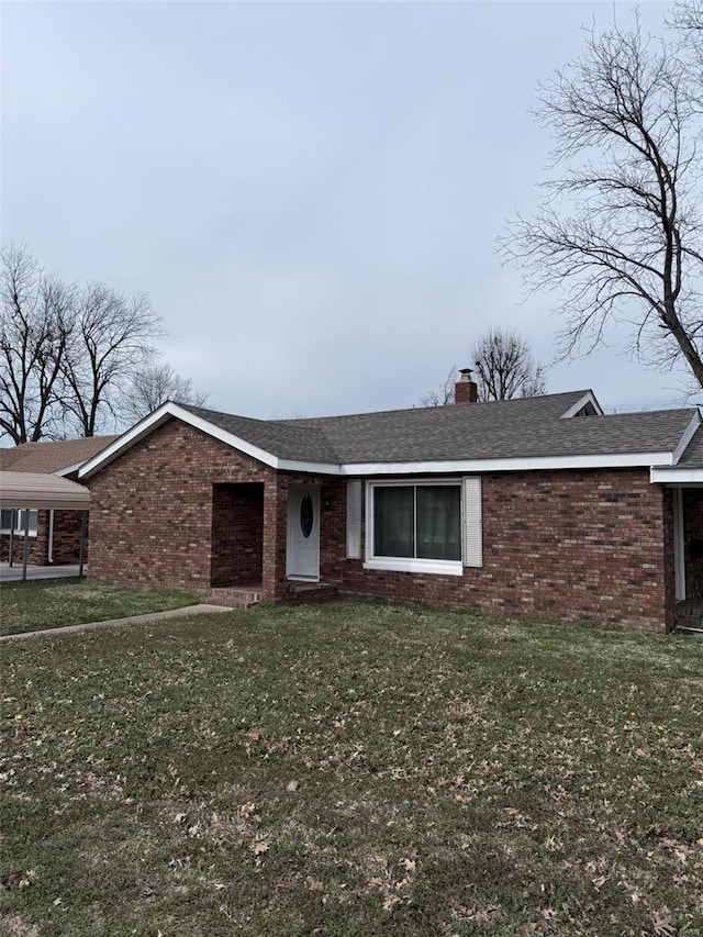 view of front facade with brick siding, a chimney, a front yard, and roof with shingles