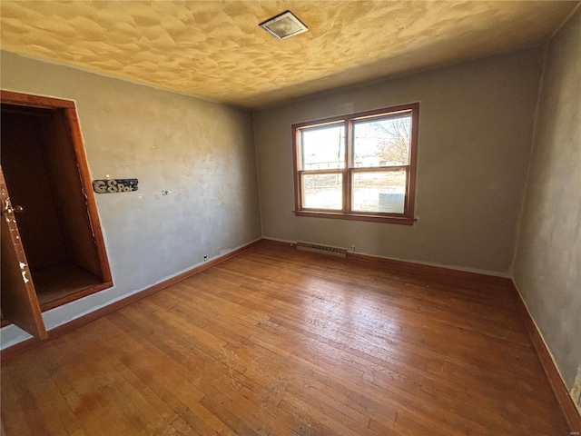 spare room with hardwood / wood-style floors, baseboards, visible vents, and a textured ceiling