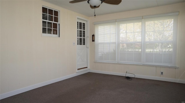 empty room featuring dark carpet, baseboards, and a ceiling fan