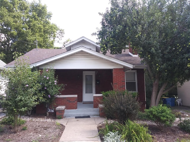 view of front facade featuring brick siding, covered porch, and a shingled roof