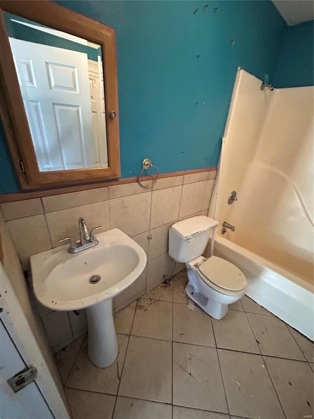 bathroom with tile patterned flooring, tub / shower combination, toilet, wainscoting, and tile walls