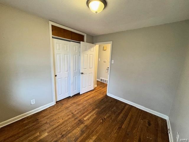 unfurnished bedroom featuring wood finished floors, baseboards, visible vents, and a closet