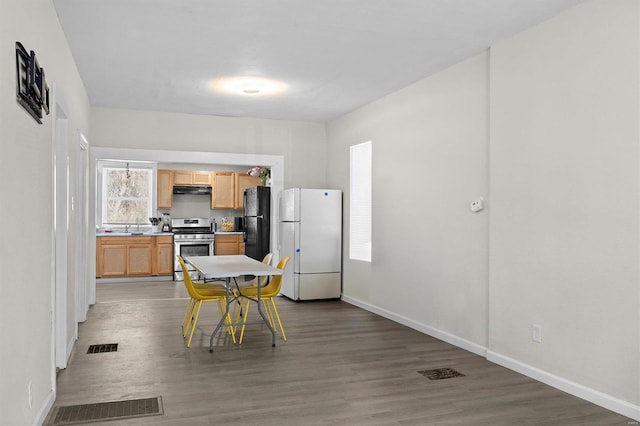 kitchen featuring stainless steel gas range oven, visible vents, freestanding refrigerator, and wood finished floors