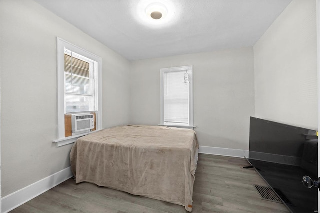 bedroom with cooling unit, wood finished floors, and baseboards