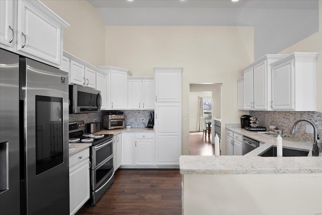 kitchen featuring dark wood-type flooring, a sink, appliances with stainless steel finishes, white cabinets, and a towering ceiling