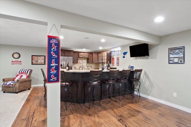 kitchen with wood finished floors, a peninsula, stainless steel fridge with ice dispenser, light countertops, and a kitchen breakfast bar