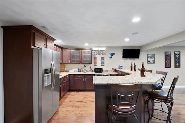 kitchen with a kitchen bar, visible vents, stainless steel refrigerator with ice dispenser, and light wood finished floors