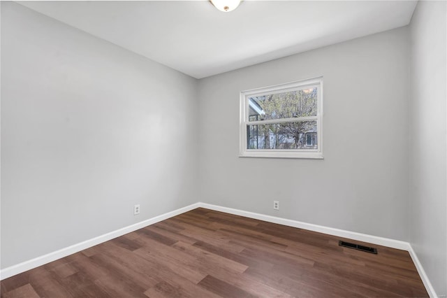 unfurnished room featuring dark wood-type flooring, visible vents, and baseboards