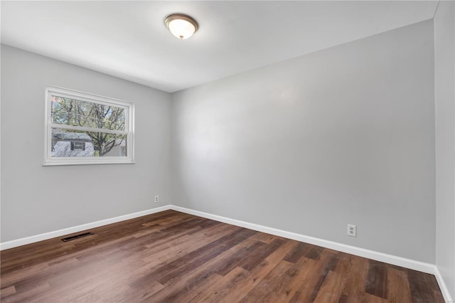 spare room featuring dark wood-type flooring, visible vents, and baseboards