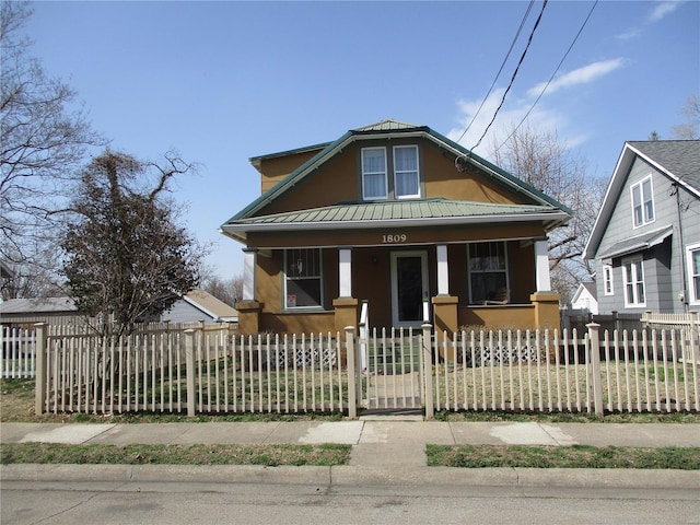 bungalow-style house featuring stucco siding, covered porch, a fenced front yard, and metal roof