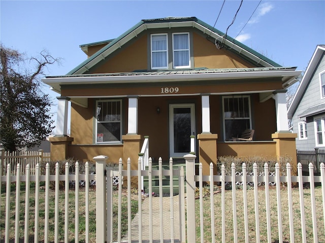 bungalow with a fenced front yard, a porch, and stucco siding