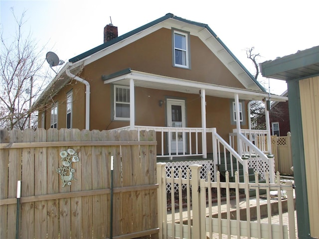 back of house with stucco siding, covered porch, a chimney, and fence