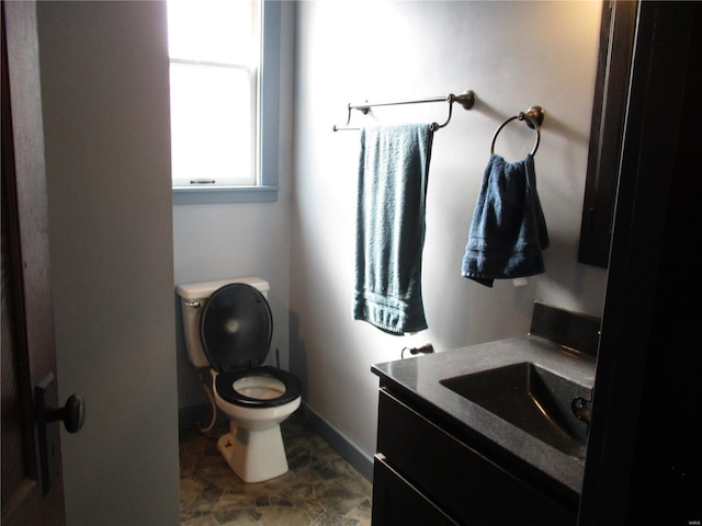 bathroom with baseboards, toilet, vanity, and stone finish floor