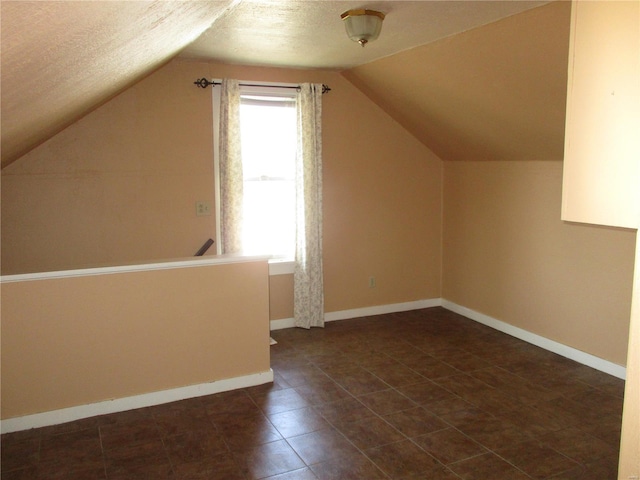 additional living space featuring lofted ceiling, baseboards, and a textured ceiling