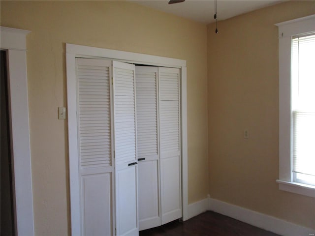 unfurnished bedroom featuring a closet, multiple windows, baseboards, and dark wood-style floors