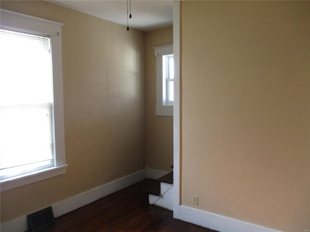 unfurnished room with visible vents, plenty of natural light, baseboards, and dark wood-style flooring