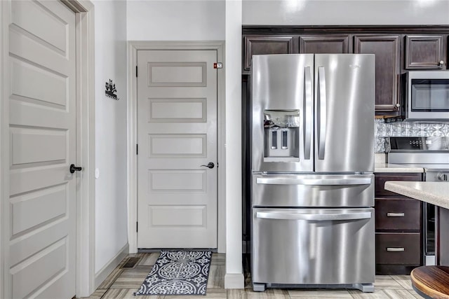 kitchen featuring stainless steel appliances, light countertops, decorative backsplash, baseboards, and dark brown cabinets