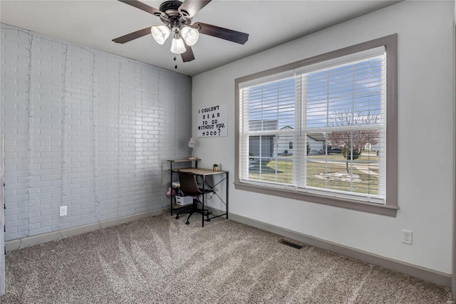 carpeted office space with visible vents, brick wall, baseboards, and a ceiling fan