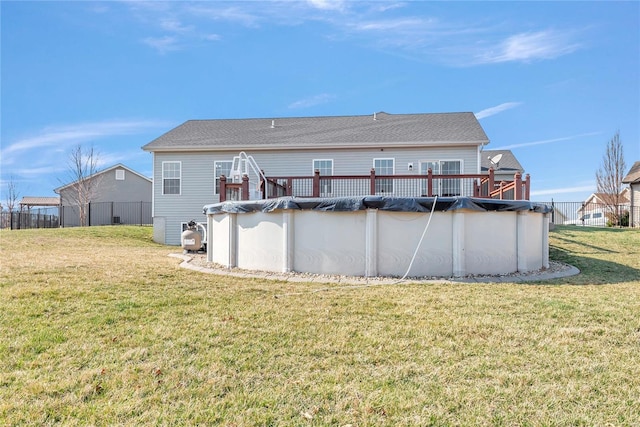 rear view of house with a deck, a covered pool, a lawn, and fence