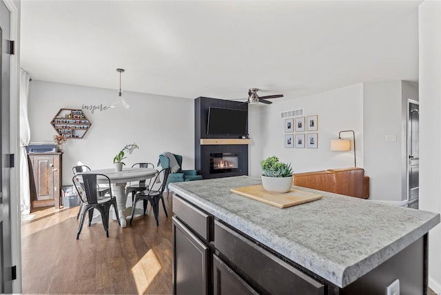 kitchen with visible vents, a large fireplace, hanging light fixtures, a ceiling fan, and dark wood-style flooring