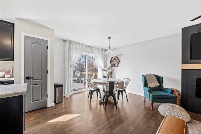 dining space with dark wood-type flooring, baseboards, and a large fireplace