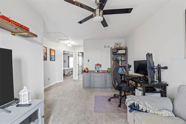 office space with visible vents, light carpet, baseboards, attic access, and ceiling fan