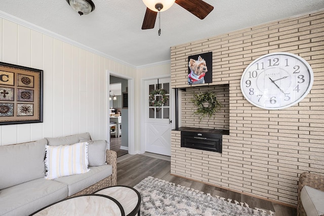 living room with wood finished floors, a ceiling fan, brick wall, ornamental molding, and a textured ceiling