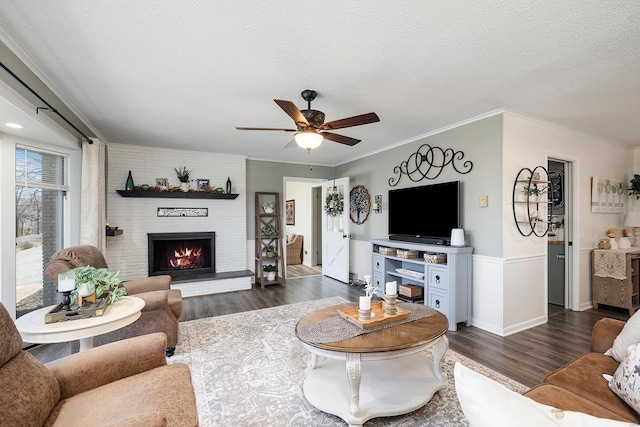 living room with crown molding, a fireplace, dark wood-style floors, a textured ceiling, and a ceiling fan