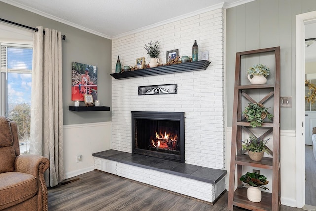 living room featuring visible vents, a brick fireplace, a wainscoted wall, ornamental molding, and dark wood-style floors