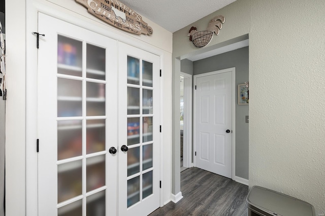 hallway with french doors, a textured ceiling, dark wood-type flooring, and a textured wall