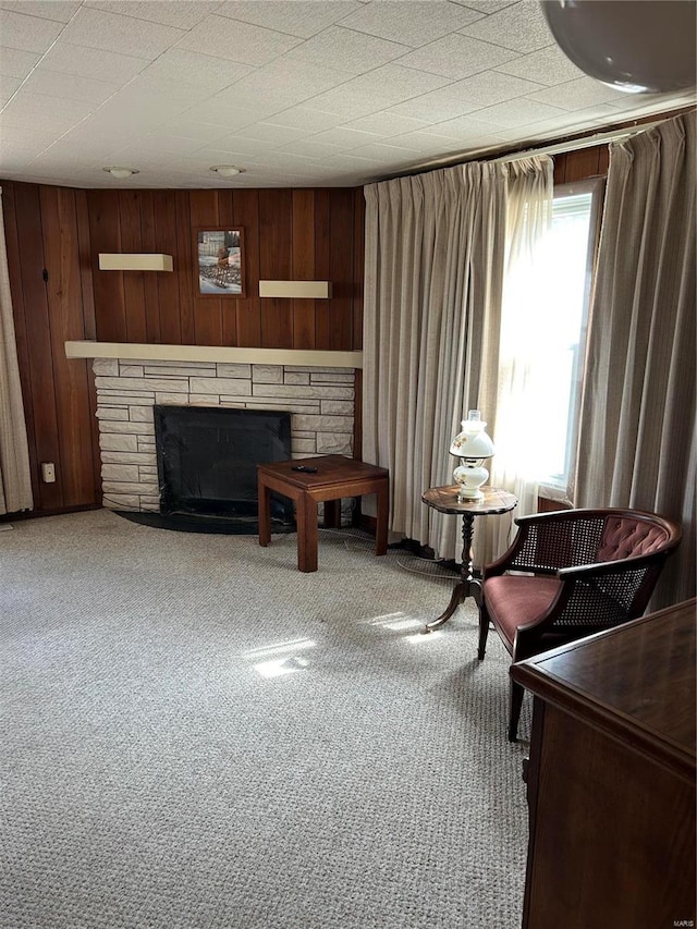 living area with carpet floors, a stone fireplace, and wood walls