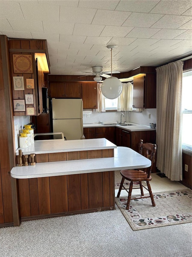 kitchen featuring a peninsula, light countertops, freestanding refrigerator, and a sink