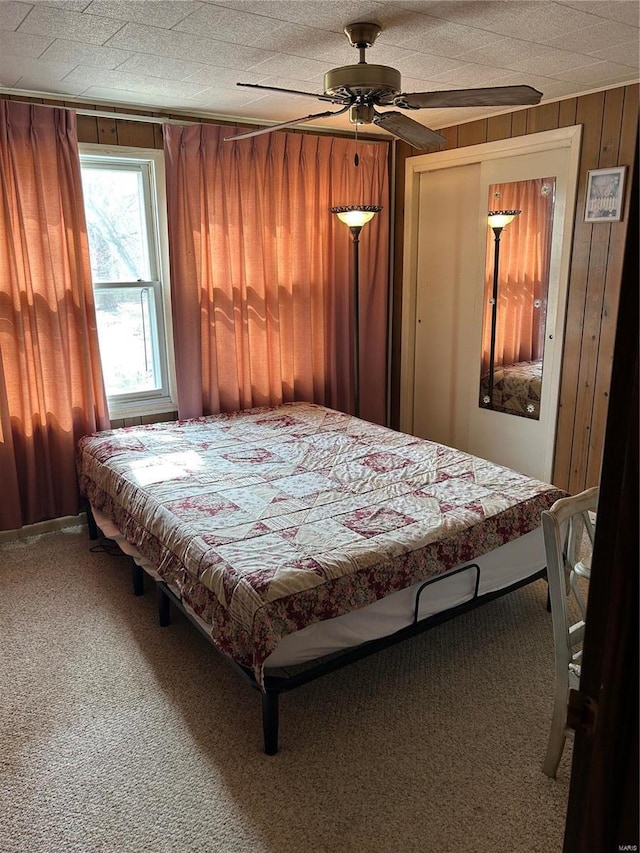 bedroom featuring a ceiling fan, wooden walls, carpet flooring, and a textured ceiling