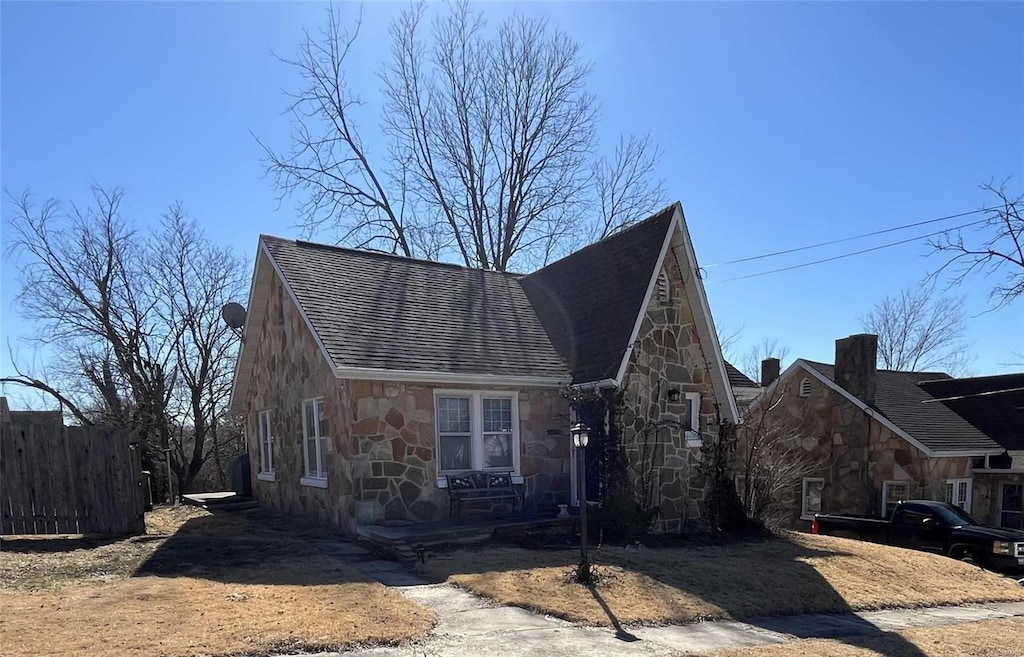 view of front of house with fence, stone siding, and a shingled roof