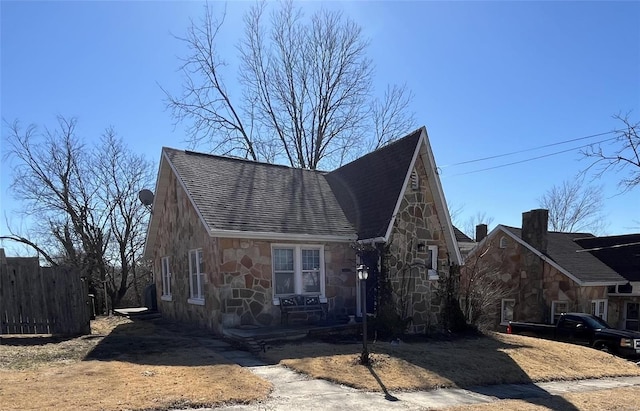 view of front of house with fence, stone siding, and a shingled roof