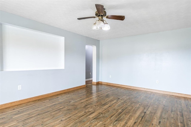 empty room with a textured ceiling, wood finished floors, arched walkways, baseboards, and ceiling fan