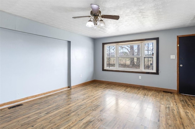 unfurnished room with baseboards, visible vents, wood-type flooring, and a textured ceiling