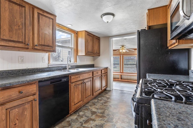 kitchen featuring brown cabinets, black appliances, a sink, dark countertops, and ceiling fan