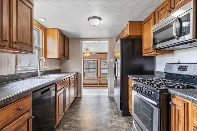 kitchen with a ceiling fan, a sink, stainless steel appliances, dark countertops, and brown cabinets