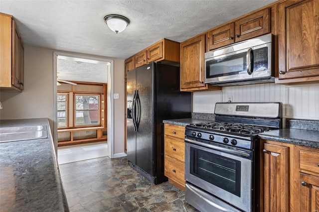 kitchen with dark countertops, stainless steel appliances, brown cabinetry, and a sink