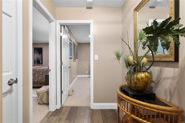 corridor featuring wood finished floors, baseboards, and a textured ceiling