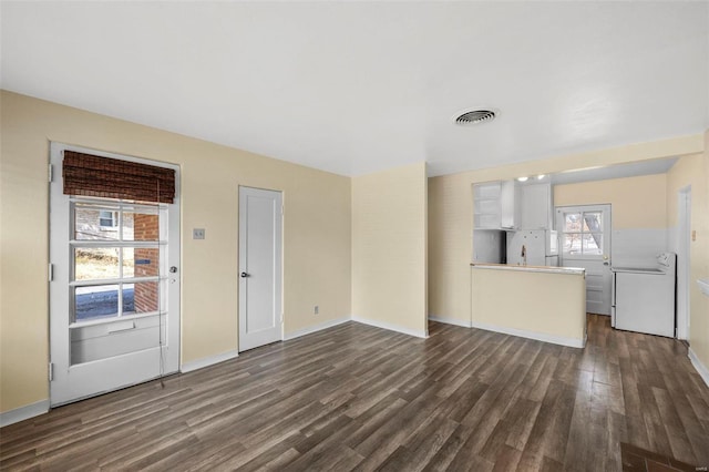 unfurnished living room with visible vents, baseboards, dark wood-type flooring, and washer / dryer