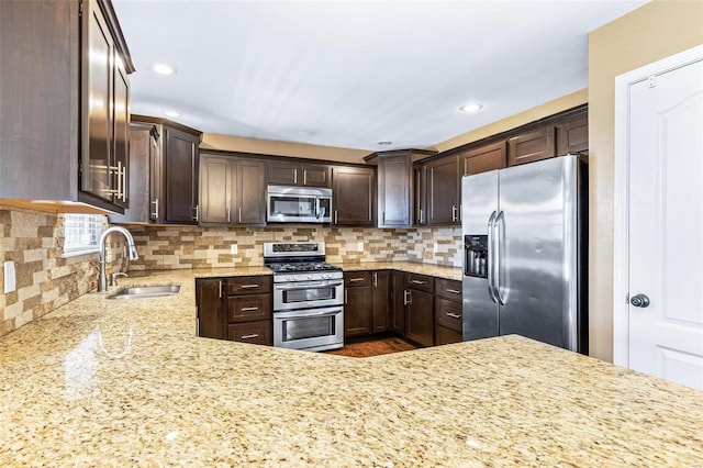 kitchen featuring a sink, dark brown cabinetry, appliances with stainless steel finishes, decorative backsplash, and light stone countertops